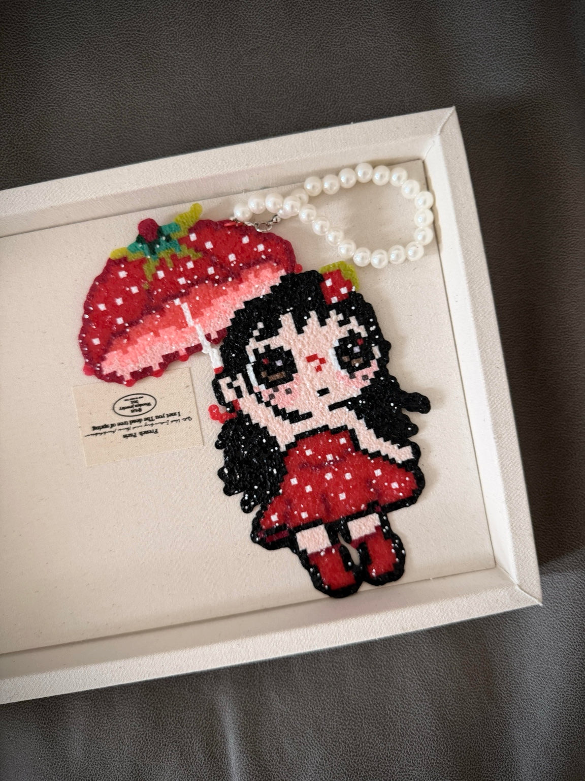 Handmade pixel bead charm featuring a girl in red with a strawberry-style umbrella