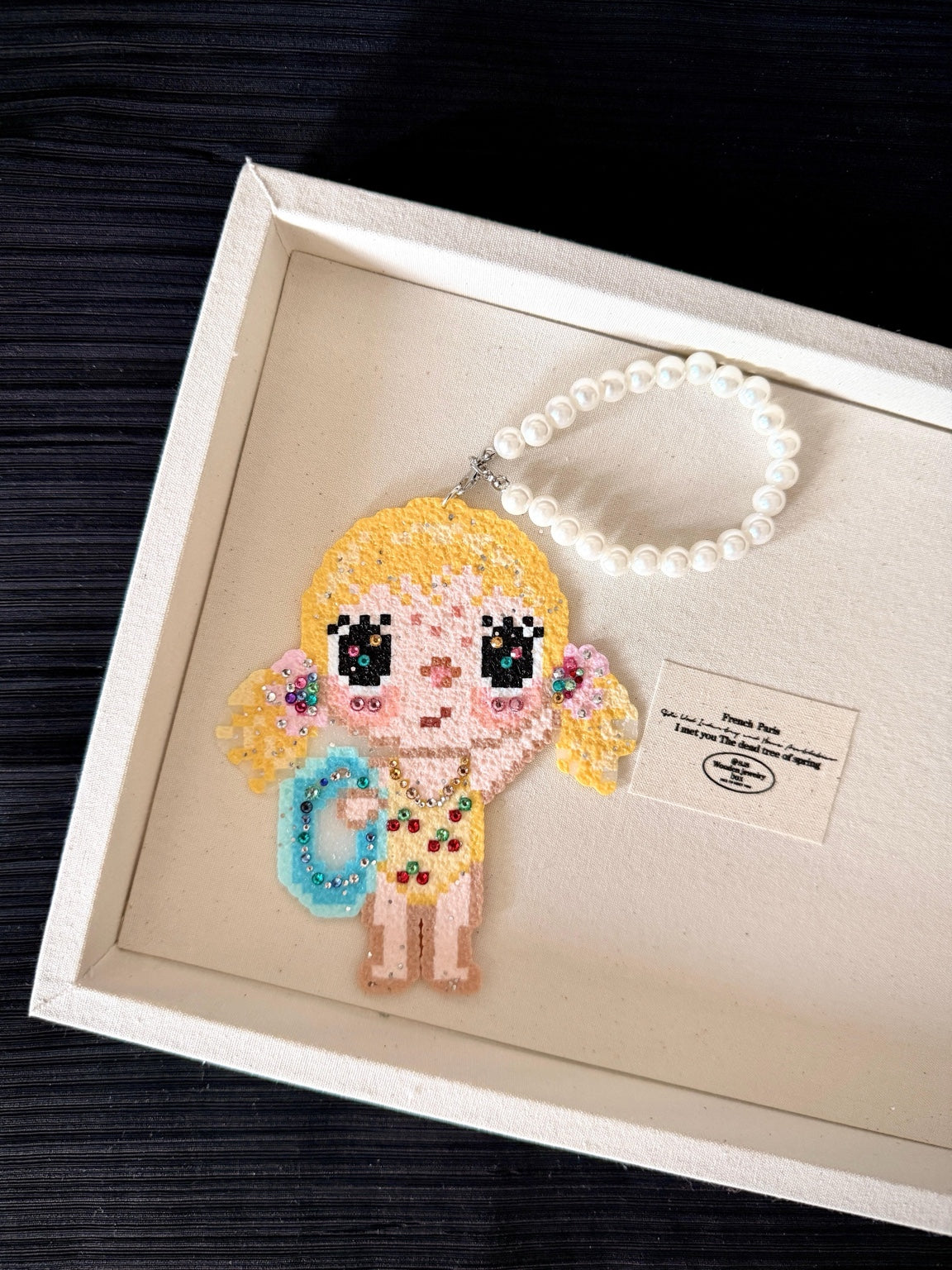 Handmade pixel bead charm featuring a blonde girl with a blue bag and sparkling details